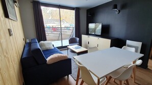 A modern living room with a sofa, a dining table, and a TV. - Appartement 2 Pieces Pied DES Pistes Proche Centre Balnéo et Randonnées (Aragnouet)