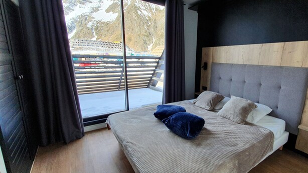 A modern bedroom with a large bed, a wooden headboard, and a view of a ski lift. - Appartement 2 Pieces Pied DES Pistes Proche Centre Balnéo et Randonnées (Aragnouet)