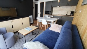 A compact living space with a sofa, a small table, a TV, and a kitchenette. - Appartement 2 Pieces Pied DES Pistes Proche Centre Balnéo et Randonnées (Aragnouet)
