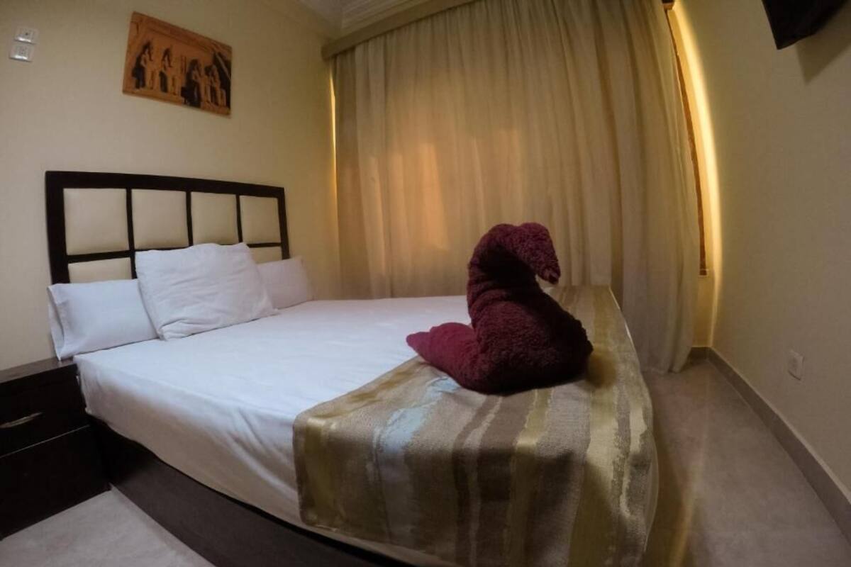 A hotel room with a bed, a dark headboard, a painting on the wall, and a window with curtains.