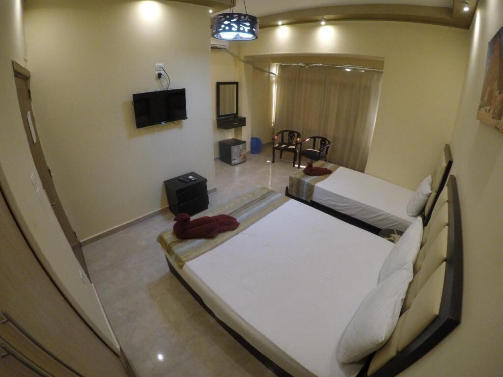 A hotel room with a large bed, a flat-screen TV mounted on the wall, a small table with a chair, and a window with curtains.