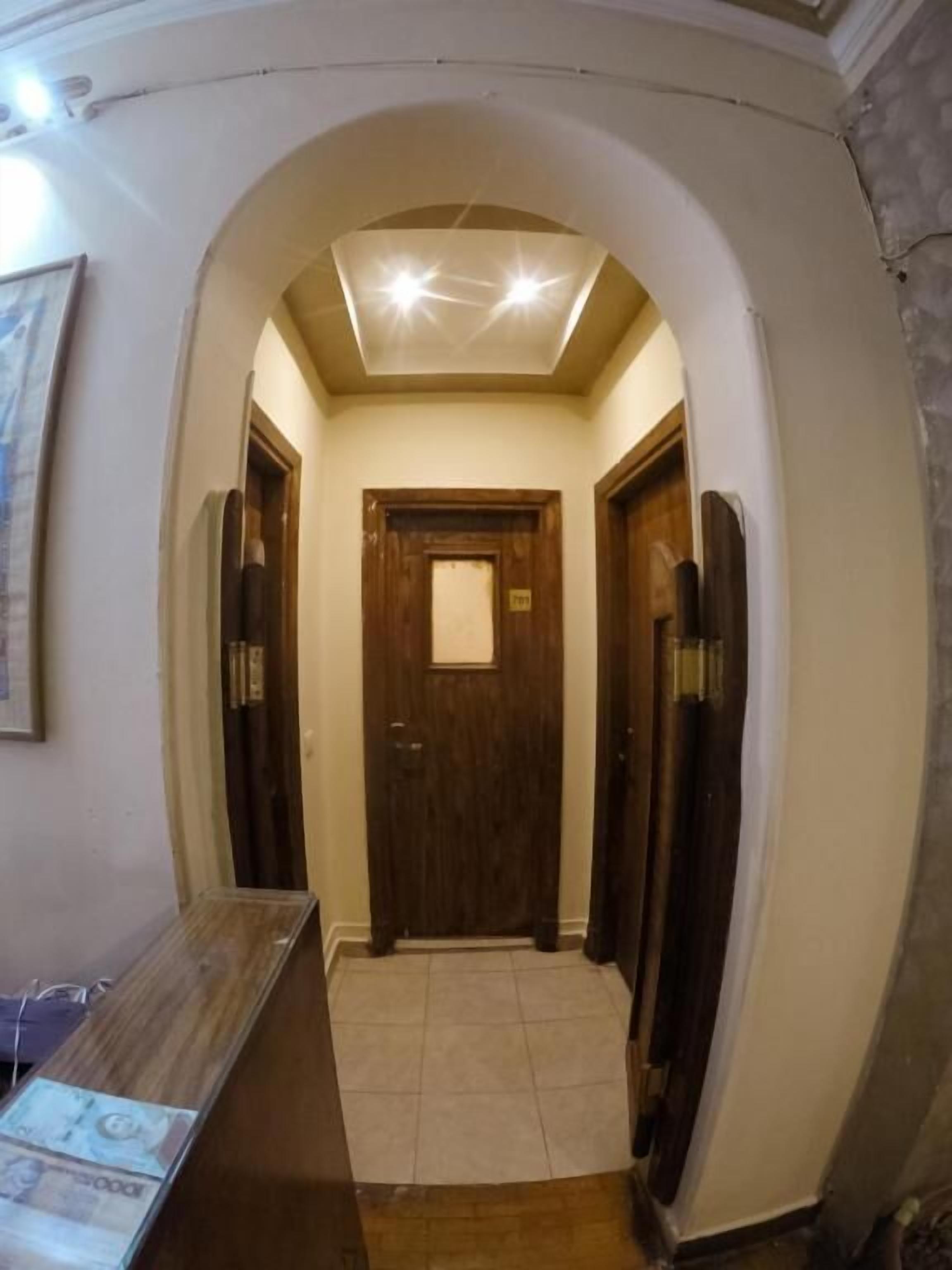 Un pasillo con una puerta de madera al final, suelo de baldosas e iluminación empotrada en el techo.