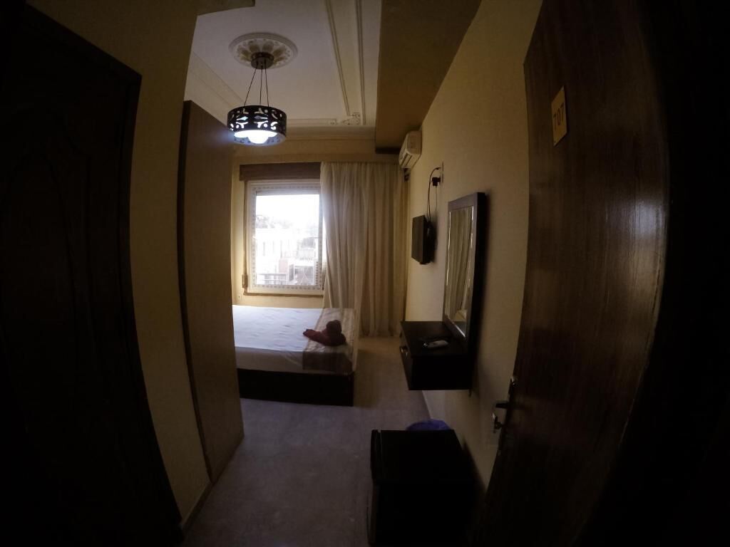 A narrow hallway with a bed, a small table, and a mirror on the wall.
