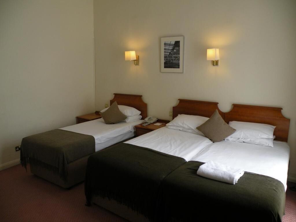 Una habitación de hotel con dos camas individuales, cada una con cabecero de madera, mesita de noche y lámpara.