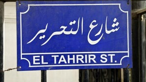 Un panneau de signalisation avec du texte en arabe et l’inscription « EL TAHRIR ST. » en dessous.