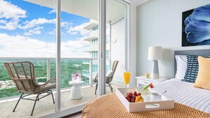 Et hotelværelse med balkon, seng, spisebord med morgenmad og stort vindue med udsigt over byen.
