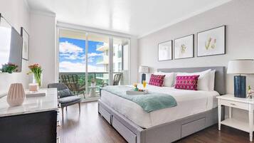 Ein modernes Hotelzimmer mit einem großen Bett, einem Schreibtisch, einem Sessel und einem Balkon mit Blick auf die Stadt.