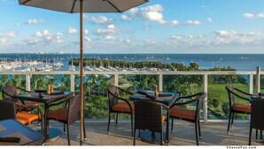 An outdoor dining area with wicker chairs and tables, overlooking a marina with numerous boats.