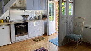 Een moderne keuken met witte kasten, een roestvrijstalen afzuigkap en een inbouwoven. Er staat een houten stoel bij de deur, en een klein vloerkleed op de vloer.