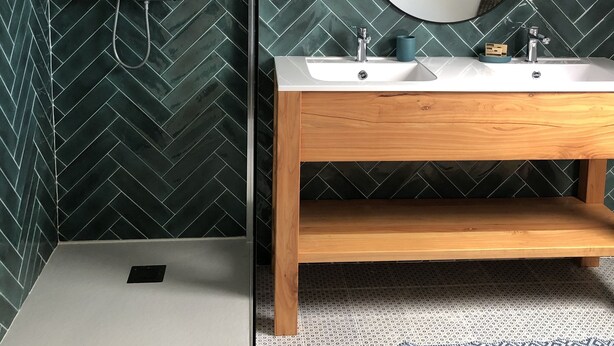 Une salle de bain avec un mur orné d’un motif en chevrons, un meuble-lavabo en bois, deux vasques, un miroir et une douche équipée d’un pommeau de douche à main.