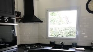 Een keuken met donkere kastjes, een ingebouwde oven, een fornuis en een raam dat voor natuurlijk licht zorgt.