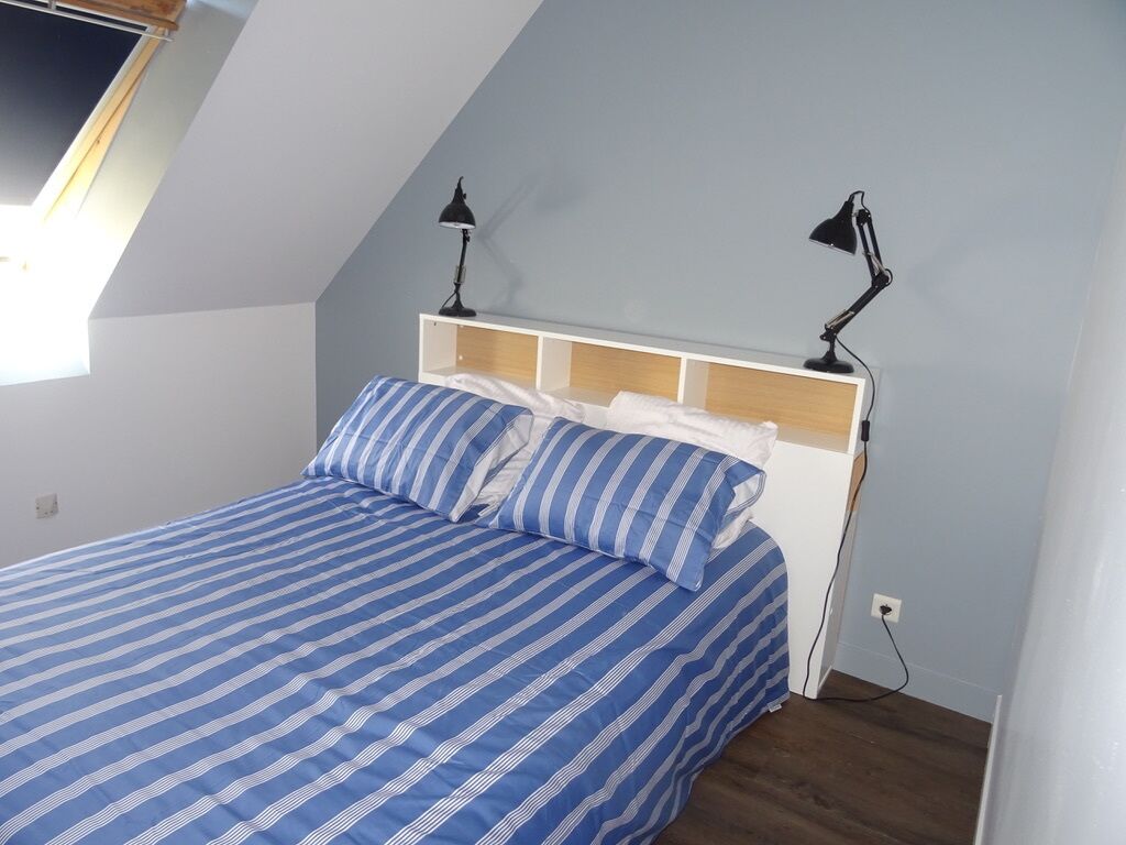 A bedroom with a sloped ceiling, a bed with striped bedding, two bedside lamps, and a power outlet on the wall.