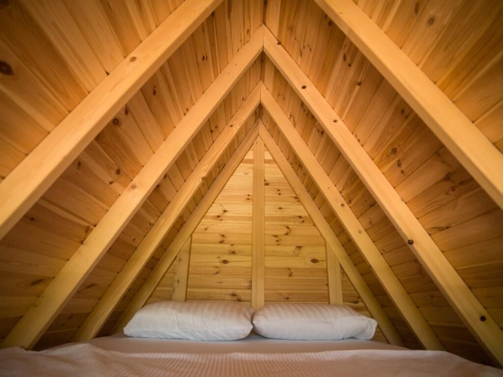 A triangular wooden ceiling with a bed at the bottom.