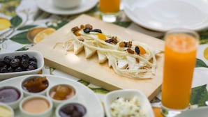 Una escena de desayuno con una tabla de madera de queso y nueces, acompañada de diversos condimentos y un vaso de jugo de naranja.