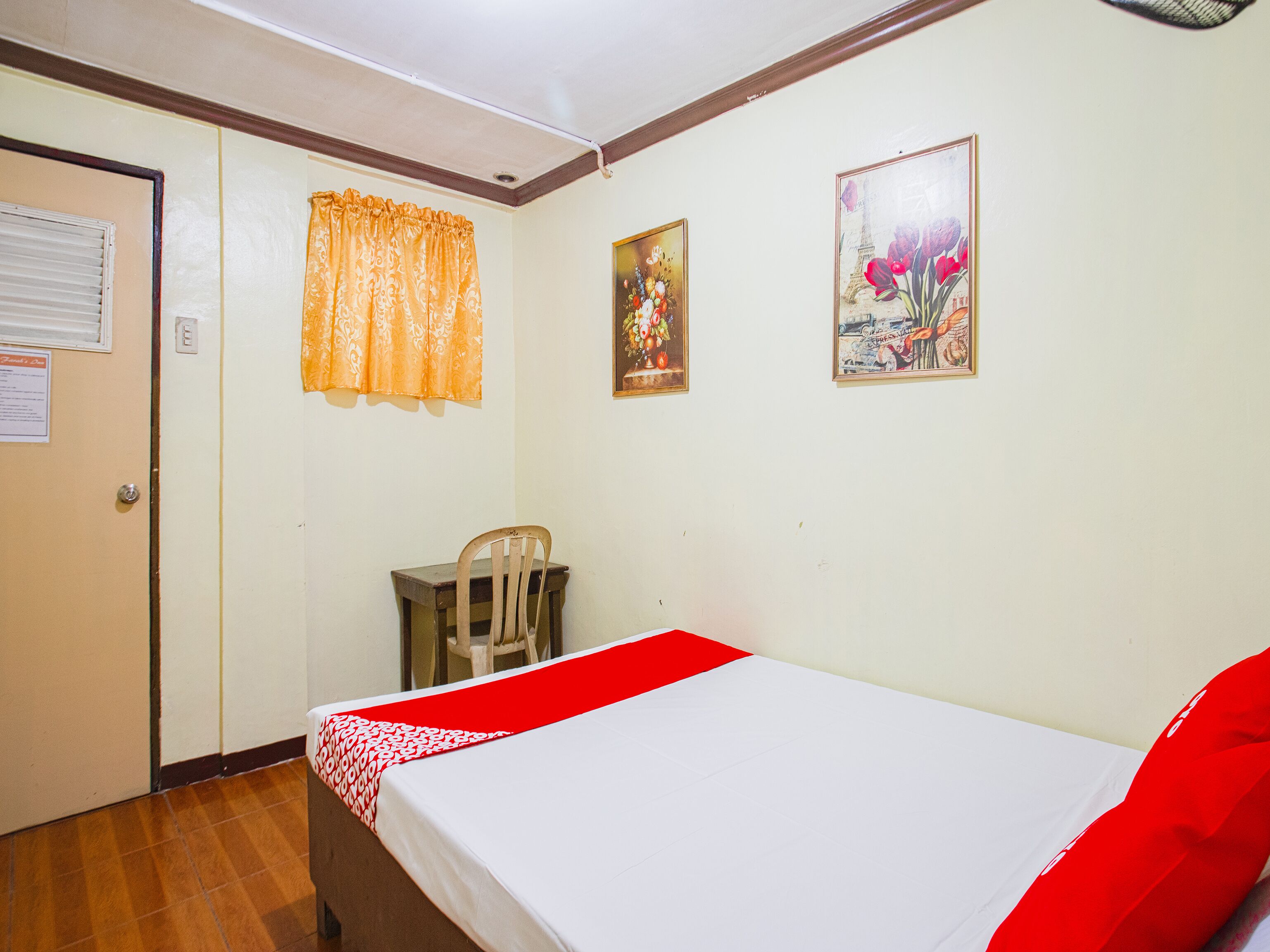 A room with a bed, a chair, and two paintings on the wall.