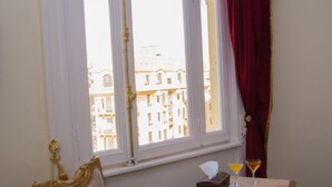 A room with a large window, a chair, a small table with a tissue box and a drink, and a red curtain. - Grand Talat Harb Plaza (Cairo)