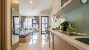 A modern kitchen with a large island, a built-in oven, and a sink. There is a dining area with a bench and a view of the city. - Bom Homes- Vinhomes Ocean Park  (Hanoi)