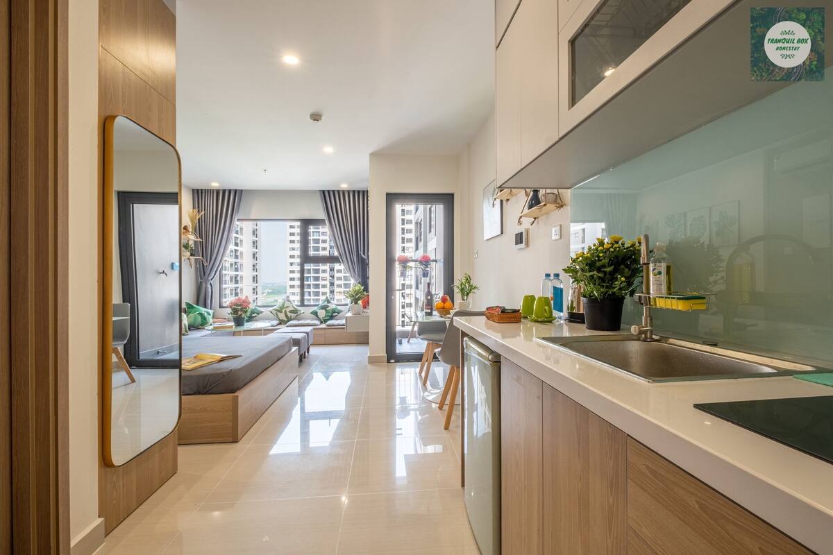 A modern kitchen with a large island, a built-in oven, and a sink. There is a dining area with a bench and a view of the city.