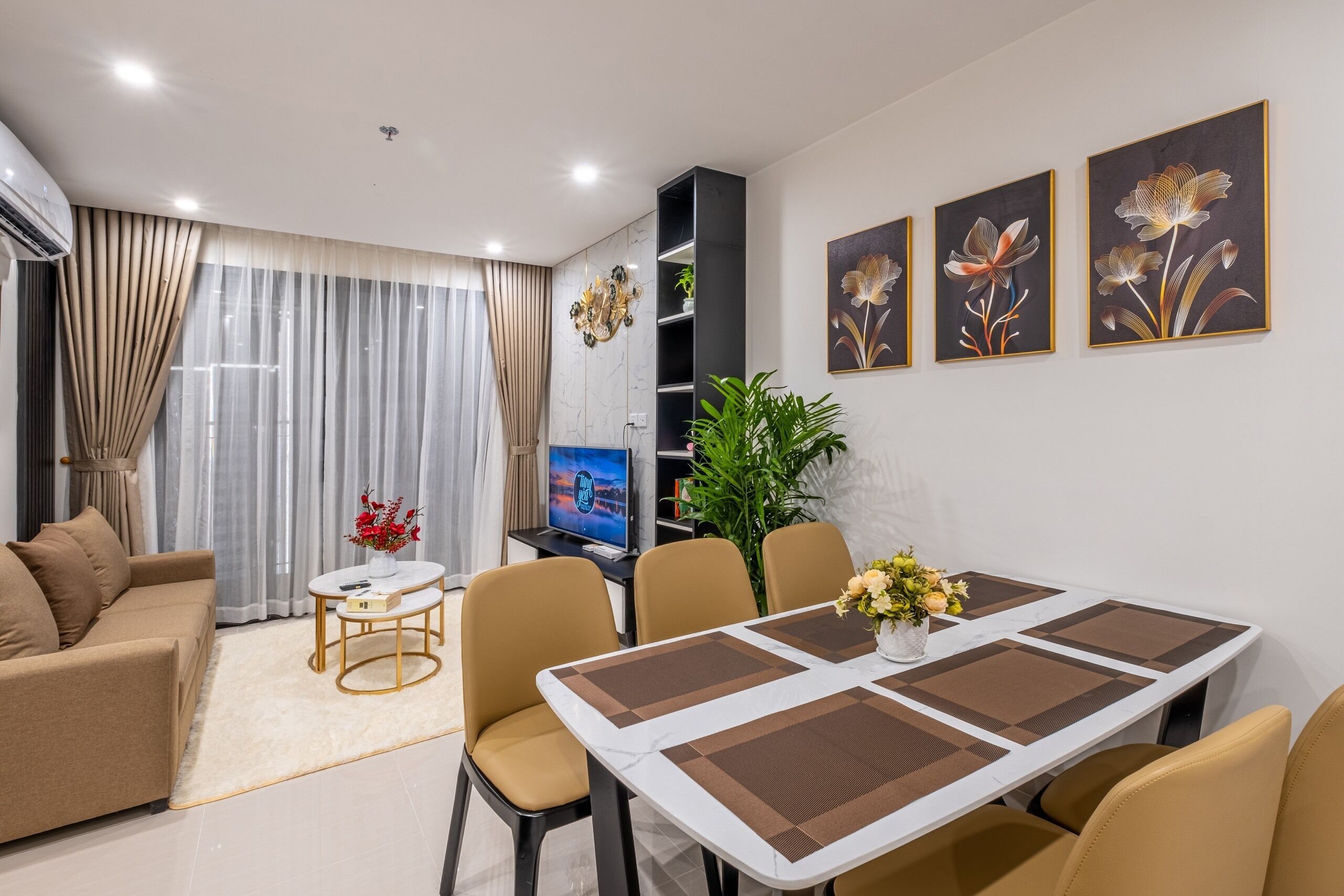 A modern living room with a sofa, a dining table with chairs, a TV, and artwork on the wall.