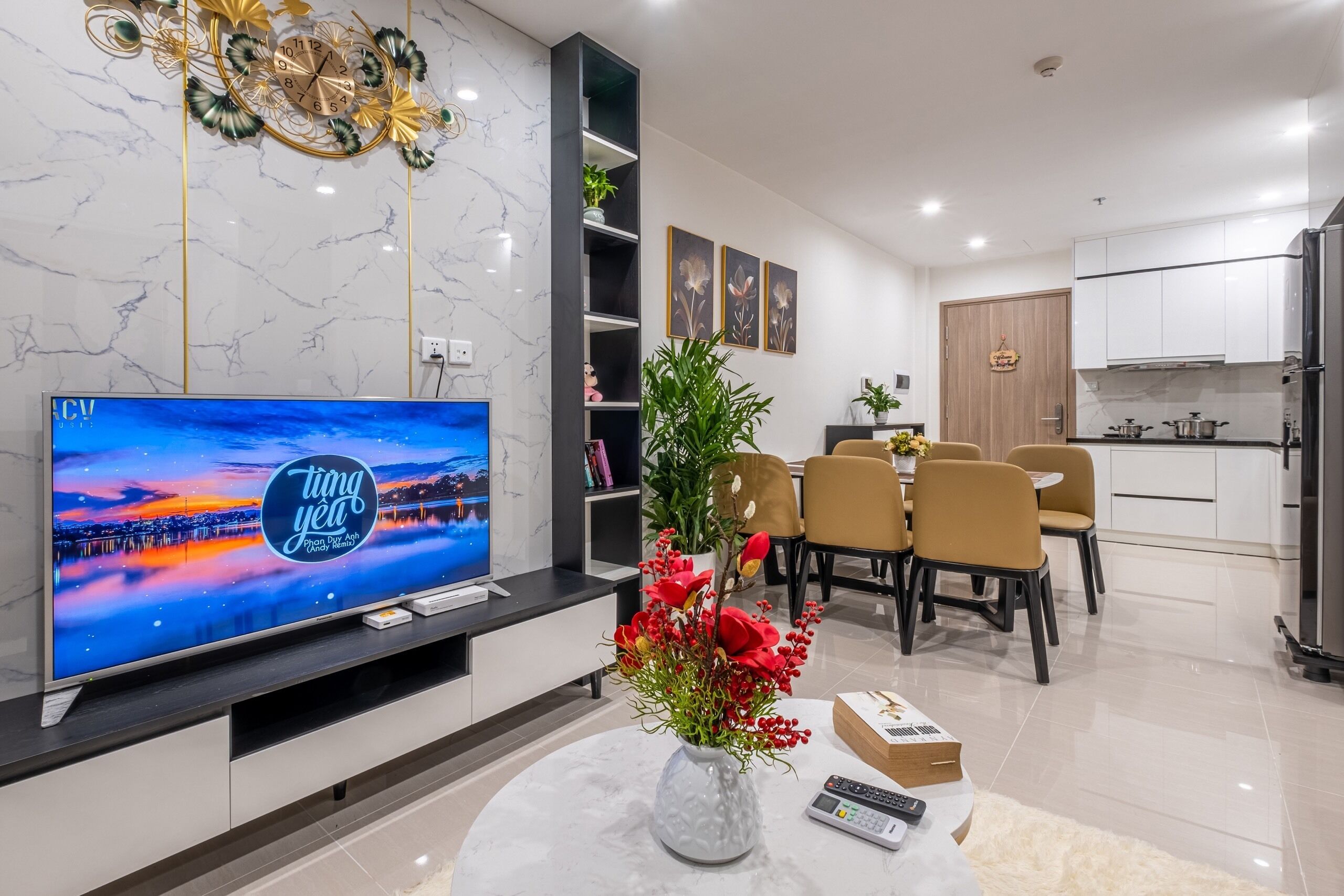Una sala de estar moderna con televisor, un reloj decorativo, una zona de comedor y una cocina.