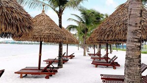 A beach with thatched umbrellas and wooden lounge chairs. - Bom Homes- Vinhomes Ocean Park  (Hanoi)