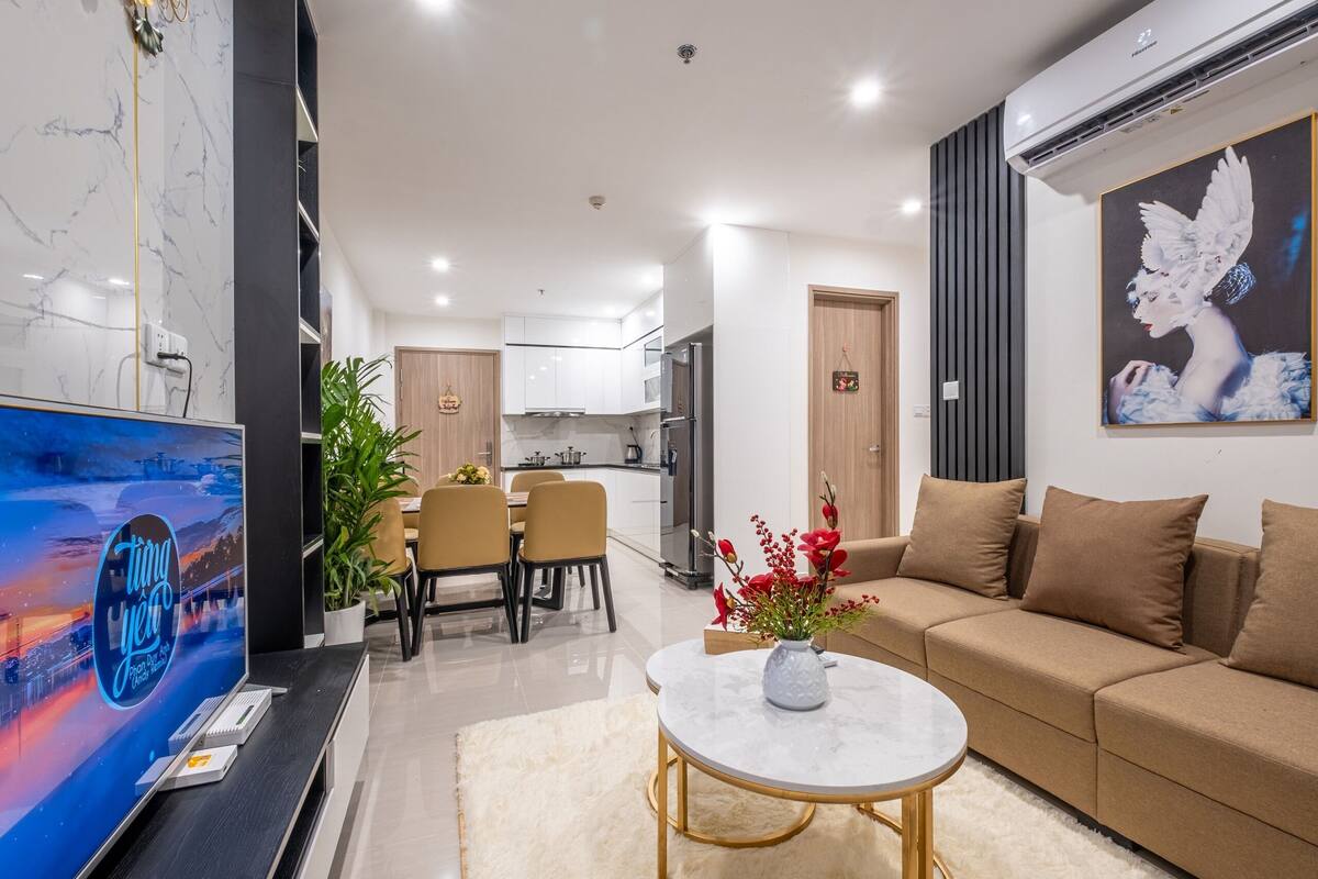 A modern living room with a flat-screen TV, a round coffee table, a beige sofa, and a dining area with chairs and a table.