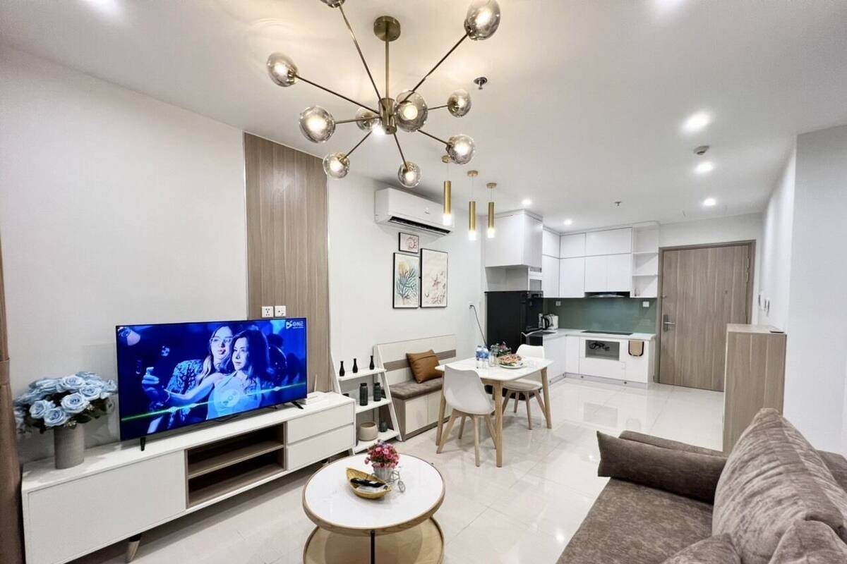 A modern living room with a flat-screen TV, a round coffee table, a sofa, and a dining area with a table and chairs.