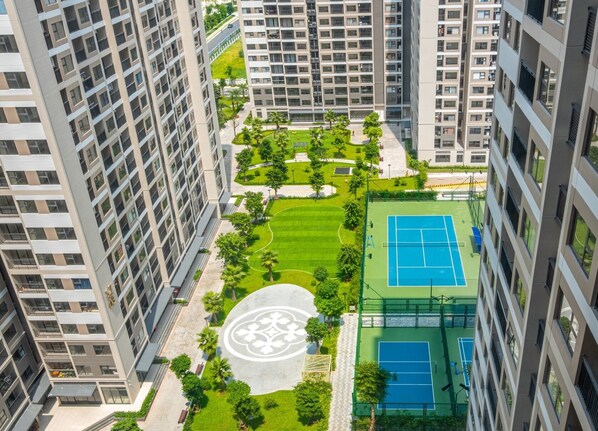 Un edificio residencial de gran altura con varios balcones, un patio central de diseño circular y una cancha de tenis.
