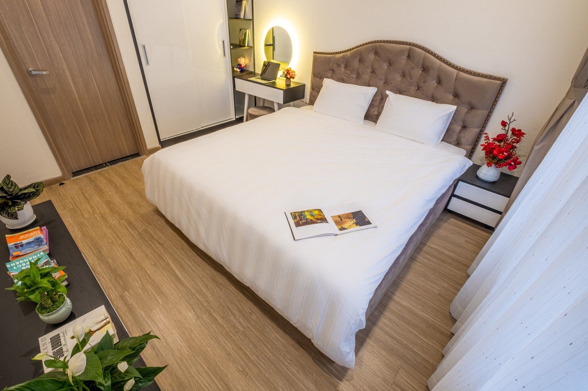 A neatly made bed with white linens, a bedside table with a lamp, and a small potted plant on the floor.
