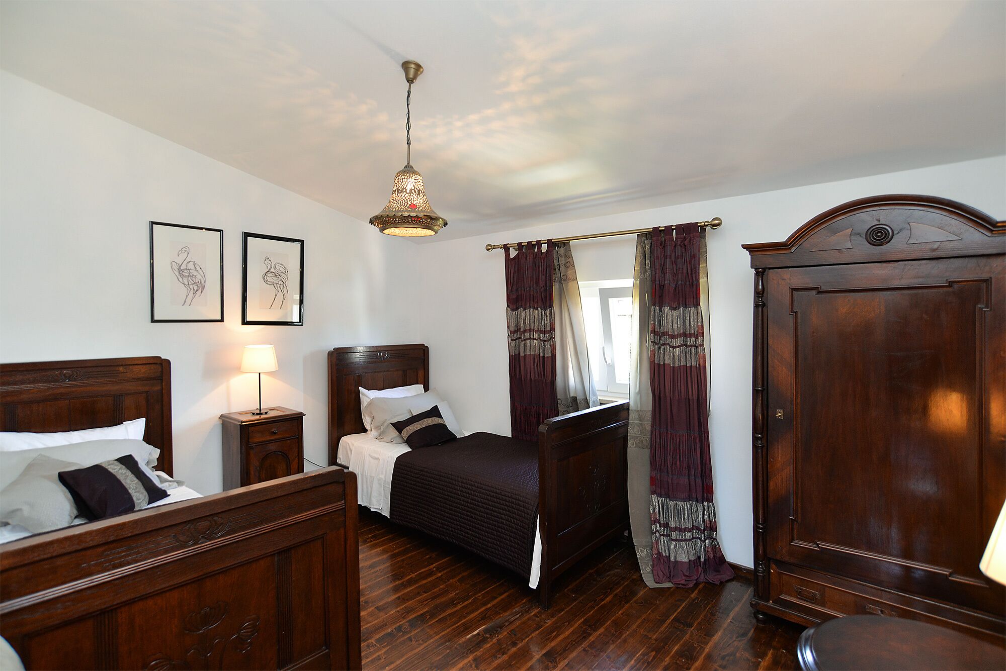 Un dormitorio con cama de madera, una mesita de noche, un armario y una lámpara colgante.
