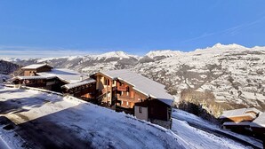 Eine Holzchalet mit schrägem Dach, umgeben von schneebedeckten Bergen und blauem Himmel.