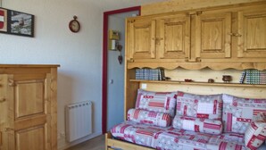 Ein Zimmer mit einem Holzkasten, einem Heizkörper und einem Bett mit gemusterten Textilien.