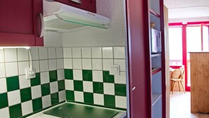 Eine Küche mit einer grün-weißen Schachbrett-Spritzschutzwand, einem Edelstahl-Spülbecken und einer roten Tür, die in einen Essbereich führt.