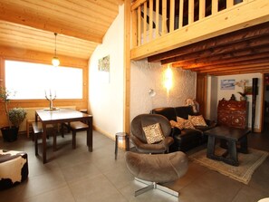 A cozy living room with a wooden ceiling, a dining area with a table and chairs, and a seating area with a sofa and armchairs.