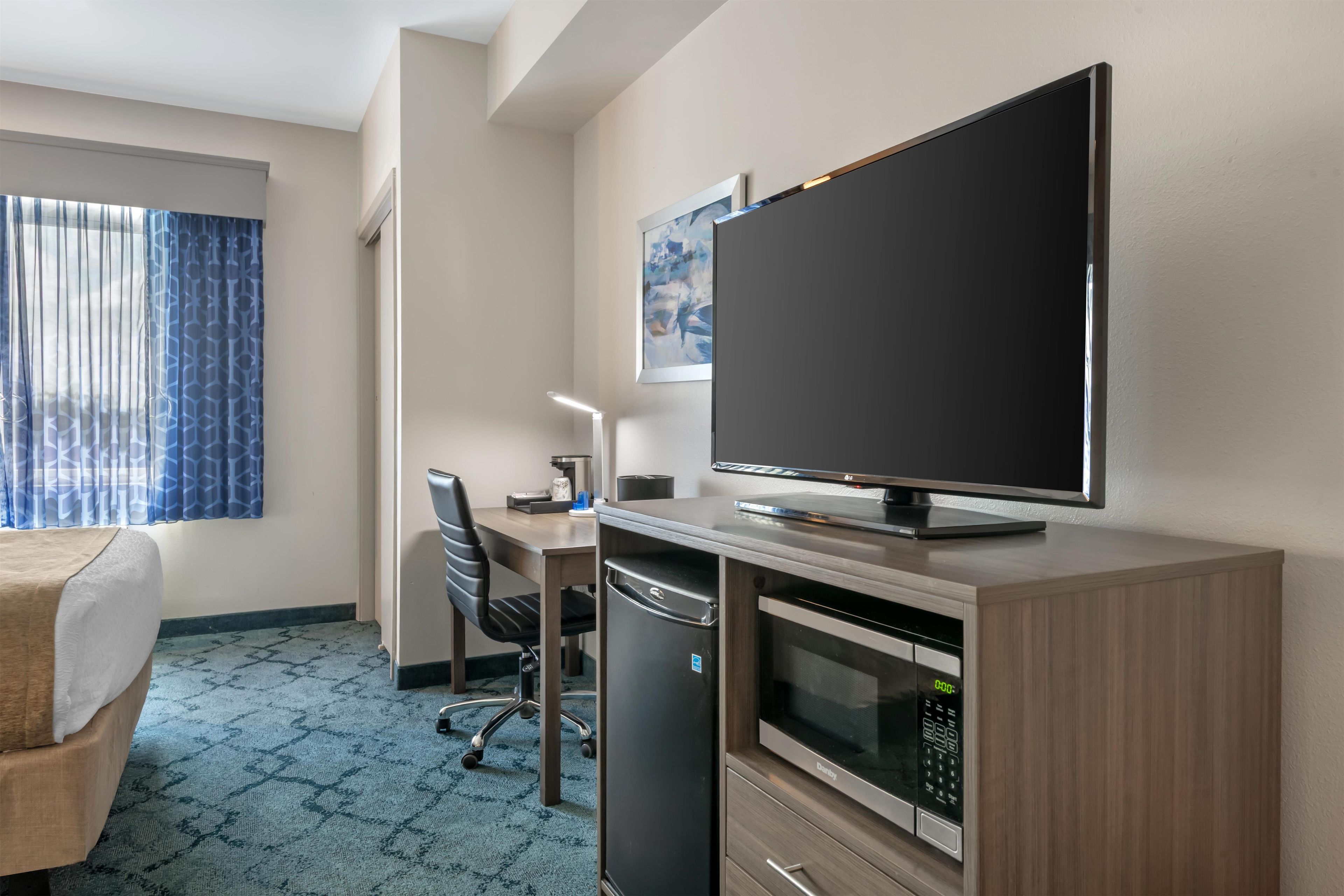 Habitación de hotel con cama, escritorio, televisor, microondas y cafetera.