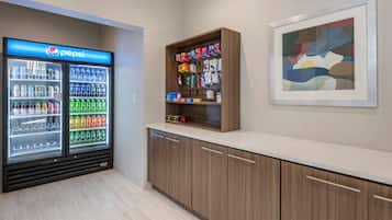 Ein Getränkeautomat mit Pepsi, ein Regal mit Snacks und ein gerahmtes abstraktes Gemälde an der Wand.