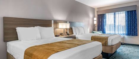 A hotel room with two beds, a desk, a lamp, and a window with curtains.
