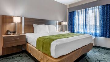 Ein Hotelzimmer mit einem großen Bett, einem Holzkopfende, zwei Nachttischen mit Lampen, einem Fenster mit blauen Vorhängen und einem gemusterten Teppich.