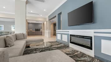 A modern living room with a sectional sofa, a glass coffee table, a fireplace, and a flat-screen TV mounted on the wall.