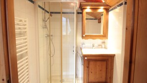 A bathroom with a glass shower enclosure, a wooden cabinet, and a mirror above the sink. - Spacious 4-room apartment well equipped with Wi-Fi and parking, at the foot of the ski bus (Les Carroz d'Arâches)