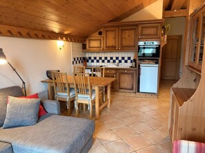 A cozy kitchen with wooden cabinets, a tiled backsplash, and a dining area with a table and chairs. - Spacious 4-room apartment well equipped with Wi-Fi and parking, at the foot of the ski bus (Les Carroz d'Arâches)