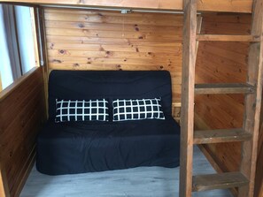 Una cabaña de madera con un sofá negro y dos almohadones cuadriculados.