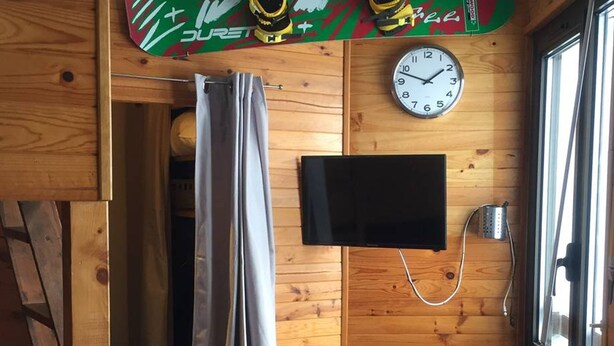 Interior de una cabaña de madera con cortina de ducha, un televisor montado y un reloj en la pared.