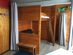 Una habitación de madera con una cama litera, un pequeño banco y una pared de madera con un letrero con motivos de esquí.