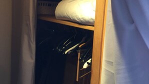 Un armario con estantes de madera, una barra para colgar y una cama con ropa de cama blanca.
