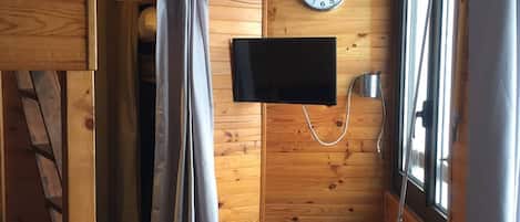 A wooden cabin interior with a shower curtain, a mounted television, and a clock on the wall.