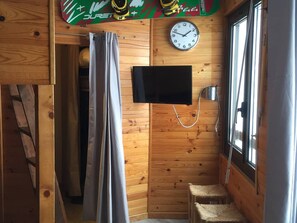 A wooden cabin interior with a shower curtain, a mounted television, and a clock on the wall.