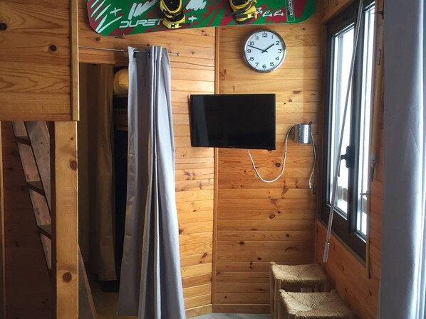 Interior de una cabaña de madera con cortina de ducha, un televisor montado y un reloj en la pared.
