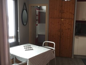 Una cocina pequeña con una puerta de madera, una mesa blanca con mantel estampado de lunares y una silla blanca.