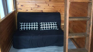 Una cabaña de madera con un sofá negro y dos almohadones cuadriculados.